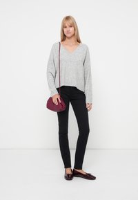 Suéter gris de cuello en V, jeans slim negros, bolso cruzado burdeos y mocasines oscuros. Textura suave, diseño casual y forma compacta del bolso.