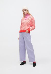 Rød og lyserød mønstret strikket sweater med V-udskæring, kombineret med lavendel vidde-buks i fløjl. Sorte sko og lyserød beanie fuldender looket.