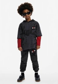 Sudadera con capucha gráfica negra con mangas largas rojas, combinada con pantalones negros estampados. Presenta diseños de telarañas y un emblema rojo. Usada con zapatos negros.