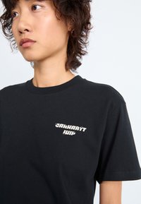 Black cotton t-shirt featuring a graphic logo in white on the left chest area. Short sleeves and a crew neckline. Smooth texture.