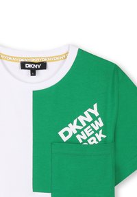 Camiseta de color verde y blanco con bloque de colores, cuello redondo, que presenta un logo gráfico en blanco y un bolsillo en la parte frontal del lado izquierdo.