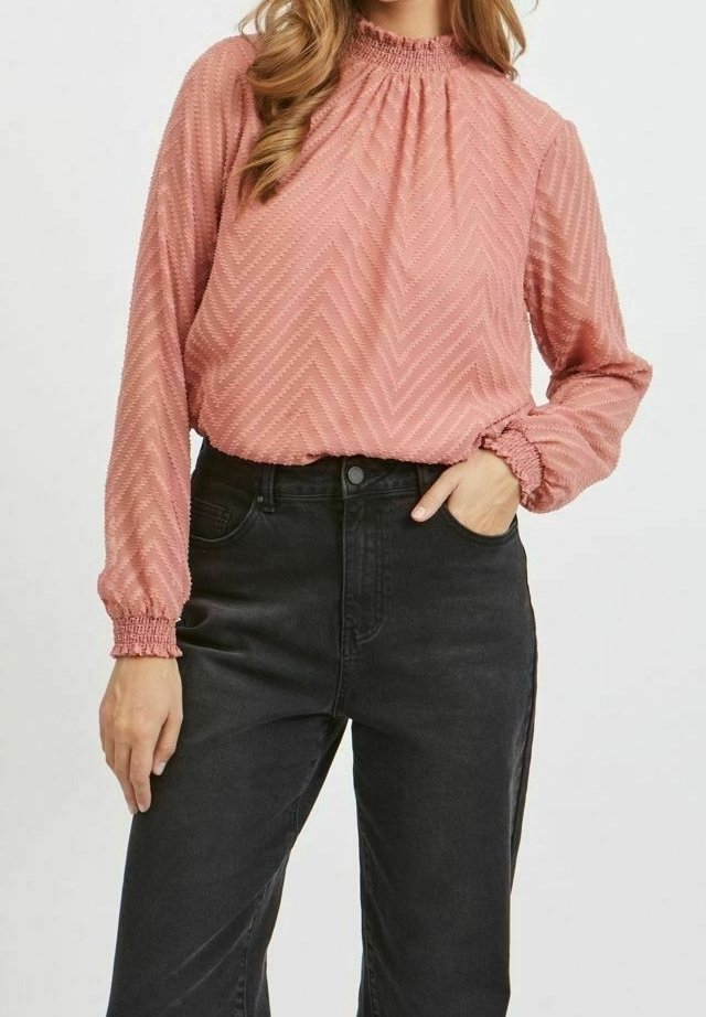 Blusa rosa polveroso con collo alto e arricciato e maniche lunghe, caratterizzata da un motivo a zigzag testurizzato, abbinata a jeans neri a vita alta.