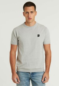 Lichtgrijze T-shirt met korte mouwen van zacht materiaal, met een ronde halslijn en een klein zwart logopatch op de borst.