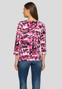 Three-quarter sleeve top in pink, black, and white geometric pattern. Made of soft fabric, featuring a round neckline and relaxed fit.
