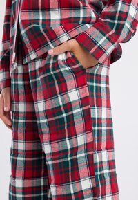 Rood en groen geruite pyjama set met witte accenten. Zachte stof, lange mouwen en zakken op de broek. Contrasterende vierkante patronen doorheen.