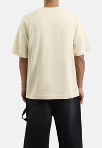 Jasnobeżowa bawełniana koszulka z luźnym krojem, okrągłym dekoltem i krótkimi rękawami, wyróżniająca się gładką teksturą i prostym wzorem.