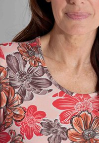 Bloemenpatroon top met rode en grijze bloemen op een lichtroze achtergrond. Gewelfde halslijn met een gestructureerde gebreide stof.