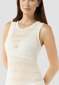 Débardeur blanc sans manches avec un design en maille texturée, présentant des motifs en losanges et des mailles ouvertes, offrant ainsi une sensation légère et respirante.