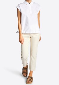 Witte blouse met korte mouwen, een kraag en een trekkoord aan de onderkant, gecombineerd met lichtbeige rechte broek en bruin dubbelgesp sandalen.