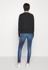 Černý svetr, modré úzké džíny a bílé tenisky. Hladká textura, ležérní design, přiléhavý tvar, viditelné švy a zadní kapsy.