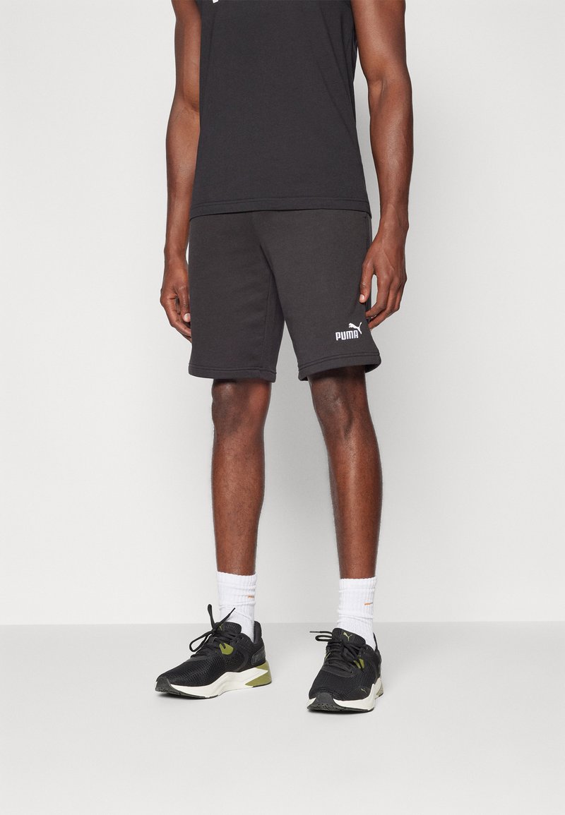 Svarte treningsshorts med elastisk midje, kombinert med svarte og grønne løpesko. Hvite sokker. Enkelt design, passende for treningsklær.
