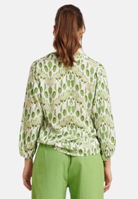 Long-sleeve blouse in a light green and white leaf pattern, featuring gathered cuffs and a relaxed fit, paired with green trousers.