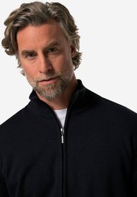 Námořnický pletený svetr na zip s vysokým límcem, texturovaným povrchem a stříbrným zipem, nošený přes bílou košili.