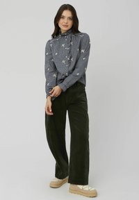 Chemise à carreaux bleue et blanche avec broderies florales, design à boutons, manches longues, associée à un pantalon large en velours côtelé vert foncé.