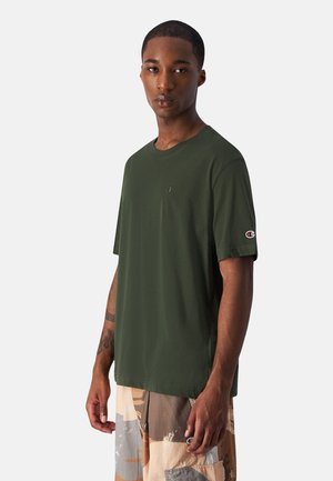 Dark green short-sleeve T-shirt made of smooth fabric. Features a small logo on the chest and a patch logo on the sleeve.
