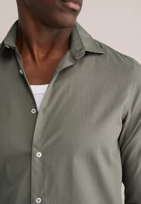 Olivno zelena srajca z gumbi in klasičnim ovratnikom, izdelana iz gladkega blaga, z belimi gumbi in subtilno teksturo.