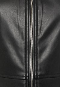 Schwarze Lederjacke mit einem sichtbaren metallischen Reißverschluss in der Mitte und strukturierter Oberfläche. Nähte betonen das Design.