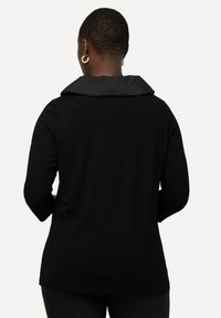T-shirt noir à manches longues avec un col noir contrastant. Tissu doux et lisse avec une coupe décontractée et un ourlet arrondi. Aucun motif ni accessoire visible.