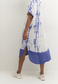 Vitt och blått tie-dye klänning, lös passform, knälång med sidofickor, textilierad tyg, korta ärmar, kombinerad med vita sneakers.