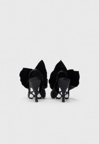 Czarne buty na wysokim obcasie z miękkiego materiału, z ostrym tyłem, falbankowym akcentem oraz podeszwą w kropki. Posiadają smukły pasek wokół kostki.