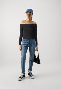 Musthave tumestatuuri musta pealelõikega topp, sinised džinsid, mustad kõrged spordijalatsid ja sinine müts. Kannab musta käekotti.