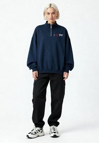 Sweat-shirt à fermeture éclair bleu marine avec le texte « I ❤️ YOU », associé à un pantalon cargo noir et des baskets blanches avec des accents noirs. Coupe et style décontractés.