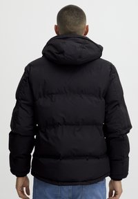 Black puffer jacket with a hood, featuring a quilted design, smooth texture, and elastic cuffs. Shown from the back with a relaxed fit.