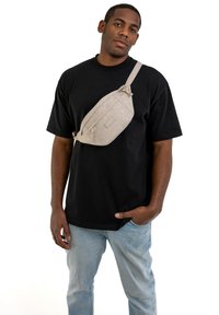 Borsa a tracolla beige realizzata in tessuto decorato, caratterizzata da un design geometrico e una tracolla regolabile, indossata sopra una t-shirt nera.
