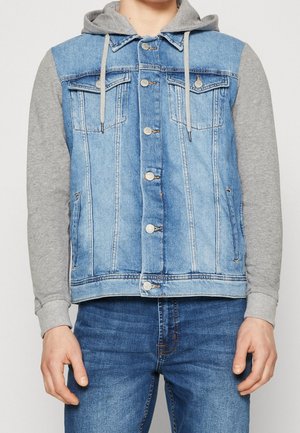 Chaleco de mezclilla con mangas de sudadera gris, tejido principal en azul claro, dos bolsillos en el pecho, cierres de botón plateados y una textura ligeramente desgastada.