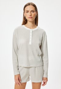 Stripet langærmet top med rund hals og knapdetaljer, parret med matchende shorts. Farve: lys beige med mørkere striber.