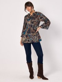 Fließende, gemusterte Bluse mit dunkelblauem, braunem und türkisfarbener Blumenmuster, mit Rüschensaum, kombiniert mit dunklen Skinny Jeans und braunen Wildleder-Stiefeln im Cowboy-Stil.