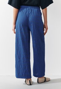 Pantalon large à motif vichy bleu avec un tissu texturé et une taille élastique, assorti à des chaussures à enfiler tissées de couleur claire.