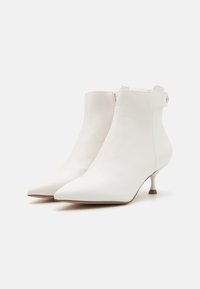 Botines de cuero blanco hasta el tobillo con punta afilada, tacón de aguja bajo y cierre de cremallera en la parte posterior, con una textura suave.