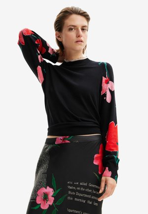Maglia nera a maniche lunghe con motivi floreali rossi sulle maniche. Presenta un collo rotondo e una silhouette aderente. Abbinata a una gonna stampata.