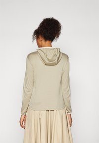 Lys beige hettegenser med en myk tekstur, som har hette og lange ermer. Plagget har en avslappet passform og diskret sømdetalj.