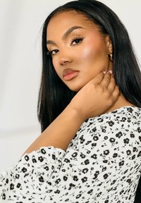 Svartvit blommig blus med lösa ärmar, mjuk textur och subtil lyster. Långt svart hår, framträdande ansiktsdrag.