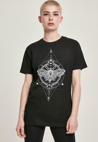 Sort bomulds T-shirt med et stort hvidt grafisk tryk af en møl og geometriske designs, med korte ærmer og rund halsåbning.