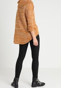 Orange och gräddfärgad melerad trikåtröja med cowl-hals, trekvartsärmar och sidoknappar, kombinerad med svarta tajta byxor och stövletter.