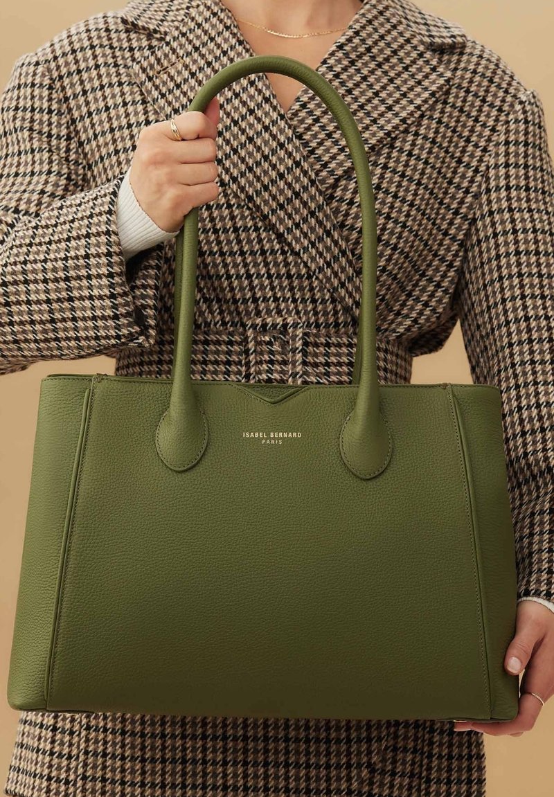 Grüne Leder-Tote-Tasche mit zwei Griffen, glatter Textur, rechteckiger Form und goldener Markenkennzeichnung auf der Vorderseite.