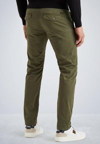Chinos vert olive avec une coupe droite, dotés de deux poches arrière à fermeture bouton et d'un tissu texturé, associés à des baskets blanches.