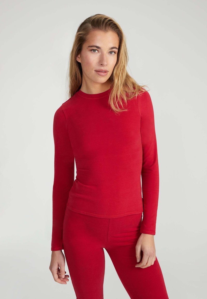 Maglietta rossa a maniche lunghe realizzata in un tessuto morbido. Caratterizzata da un colletto rotondo e un design aderente, abbinata a leggings rossi coordinati.