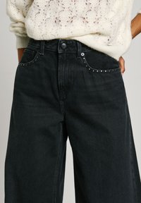 Mustad denim laiad sääred teksad dekoratiivsete hõbedaste nupukestega taskutes, klassikalise viie tasku disainiga ja sileda, tekstuurse viimistlusega.