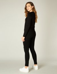 Zwarte lange mouw top gecombineerd met zwarte leggings, beide gemaakt van een gladde stof, aangevuld met witte platform sneakers.