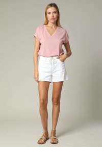 T-shirt rose à col en V avec des manches courtes, associé à un short blanc à cordon de serrage. L'ensemble présente une coupe décontractée et un tissu confortable.