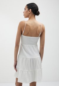 Abito bianco a strati realizzato in tessuto testurizzato, con sottili spalline regolabili e un corpetto smock, che mostra una silhouette rilassata.