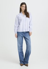 Blouse rayée bleu clair et blanc avec un col à volants et des manches longues. Associée à un jean bleu clair à jambes droites et des chaussures marron.