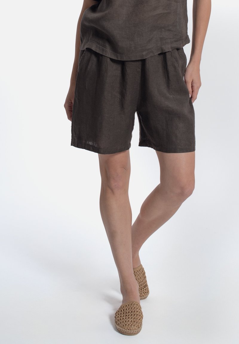 Pantaloni corti di lino marroni con vestibilità comoda, vita elasticizzata e tasche laterali. Abbinati a un top coordinato e espadrillas in paglia beige intrecciata.