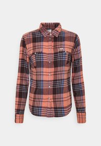 Chemise en flanelle à carreaux orange, marron et bleu marine. Elle possède deux poches poitrine, une fermeture boutonnée sur le devant et des manches longues avec des poignets boutonnés.