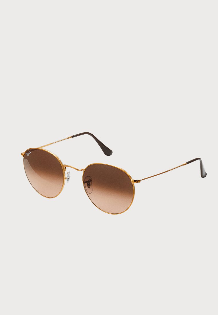 Occhiali da sole in metallo dorato con montatura rotonda, lenti gradienti marroni e bracci accentati in nero. Design leggero con un'estetica minimalista.
