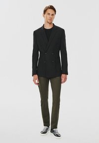 Czarna, dwurzędowa marynarka z dwoma przednimi kieszeniami, w połączeniu z oliwkowymi spodniami slim-fit i czarno-białymi sneakersami.